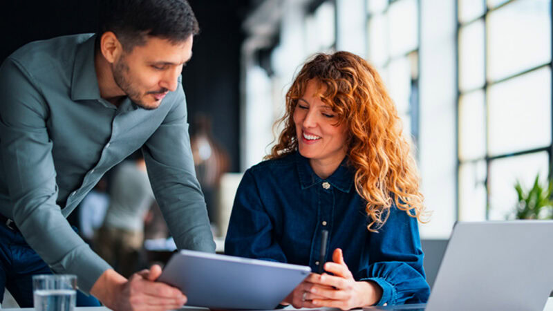 A manager and employee discussing information on a tablet in a bright, modern office during a conversation about workplace safety and workers’ compensation.